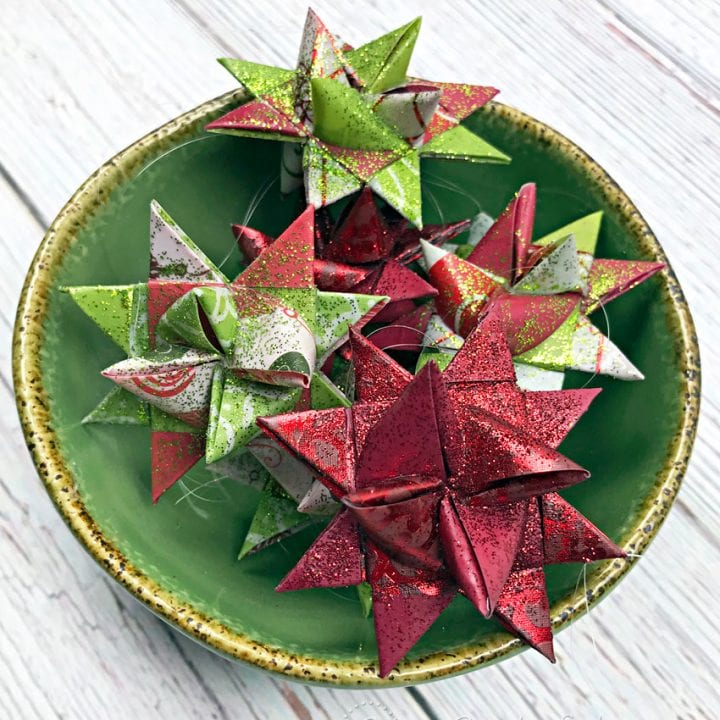 Green bowl filled with folded Froebel Star ornaments on wood table.